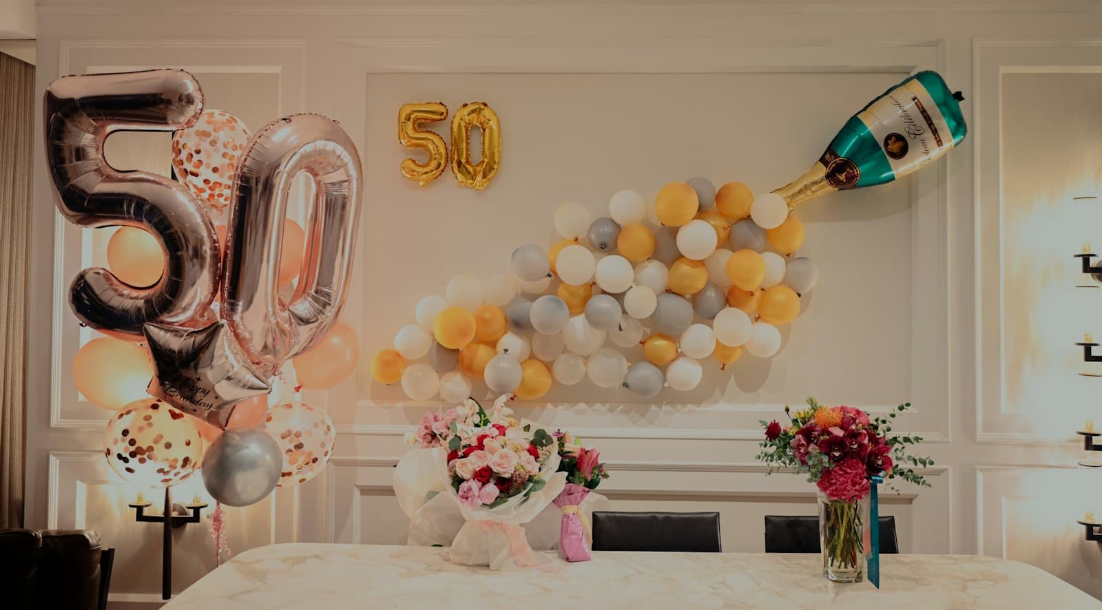 Anniversary backdrop with gold 50 balloons, a champagne-bottle balloon display and flowers