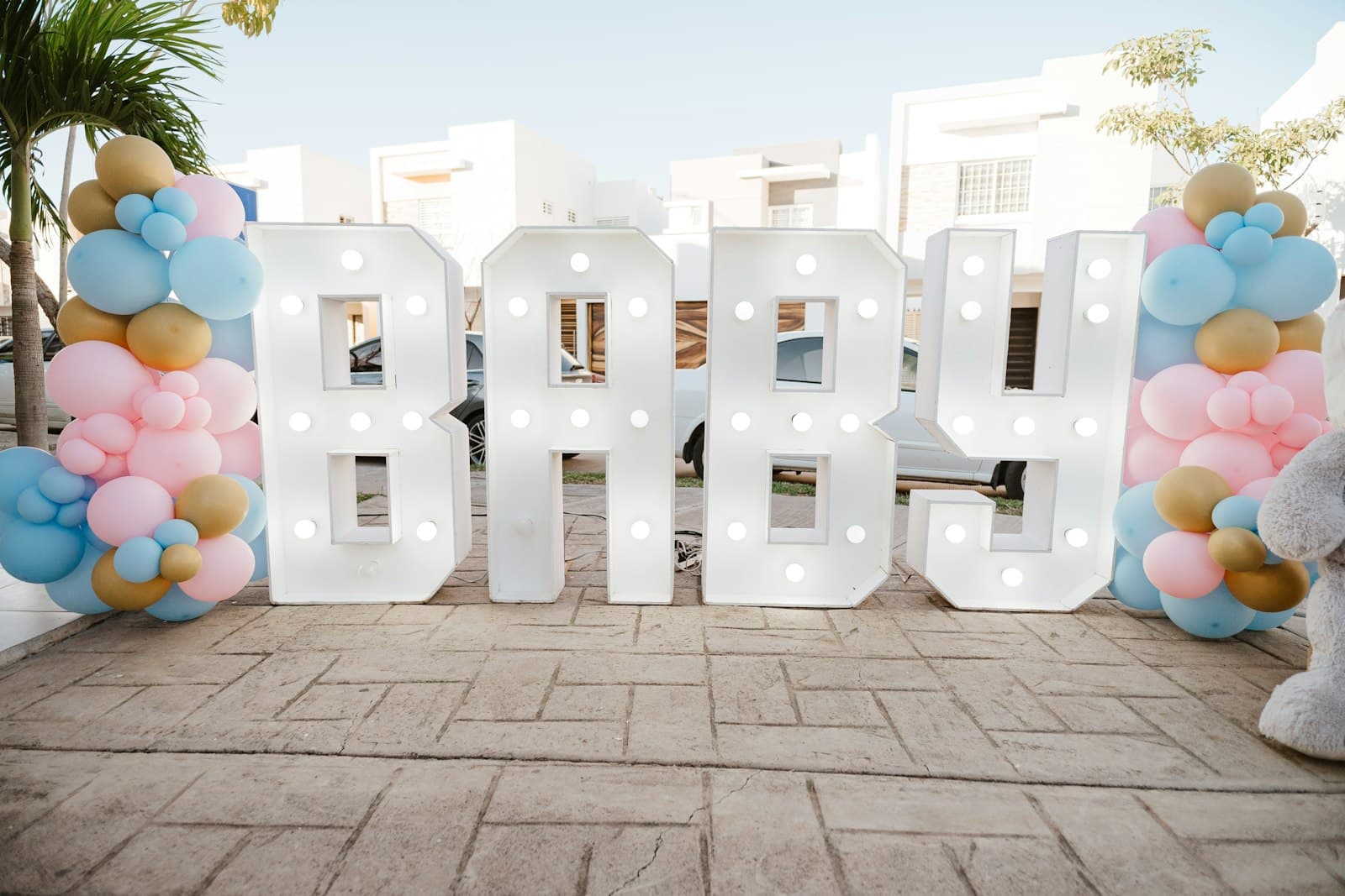 Light-up letters spelling BABY framed by pastel pink, blue and gold balloons