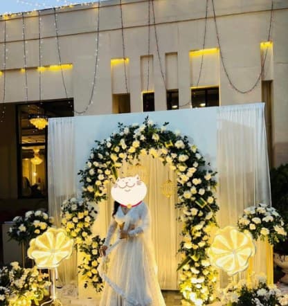 White and green floral arch with lit flower lamps against white drapes