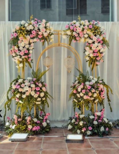 Two gold arches with pink and white flowers and hanging crystal lanterns