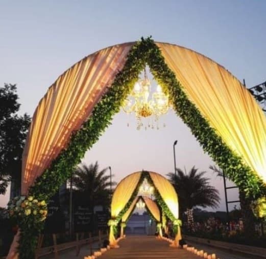 Domed gold-fabric tunnel edged with greenery and a chandelier at dusk