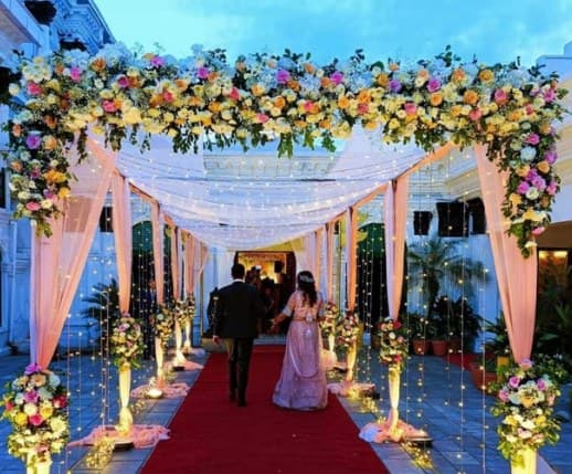 Red-carpet walkway under a pastel floral canopy with draped fabric and lit flower stands