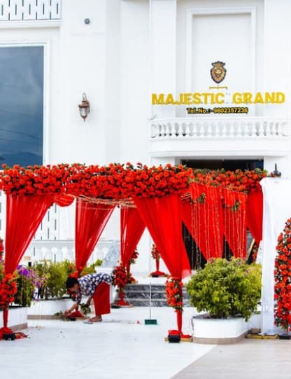 Pergola entrance of red drapes topped with red roses outside a white venue