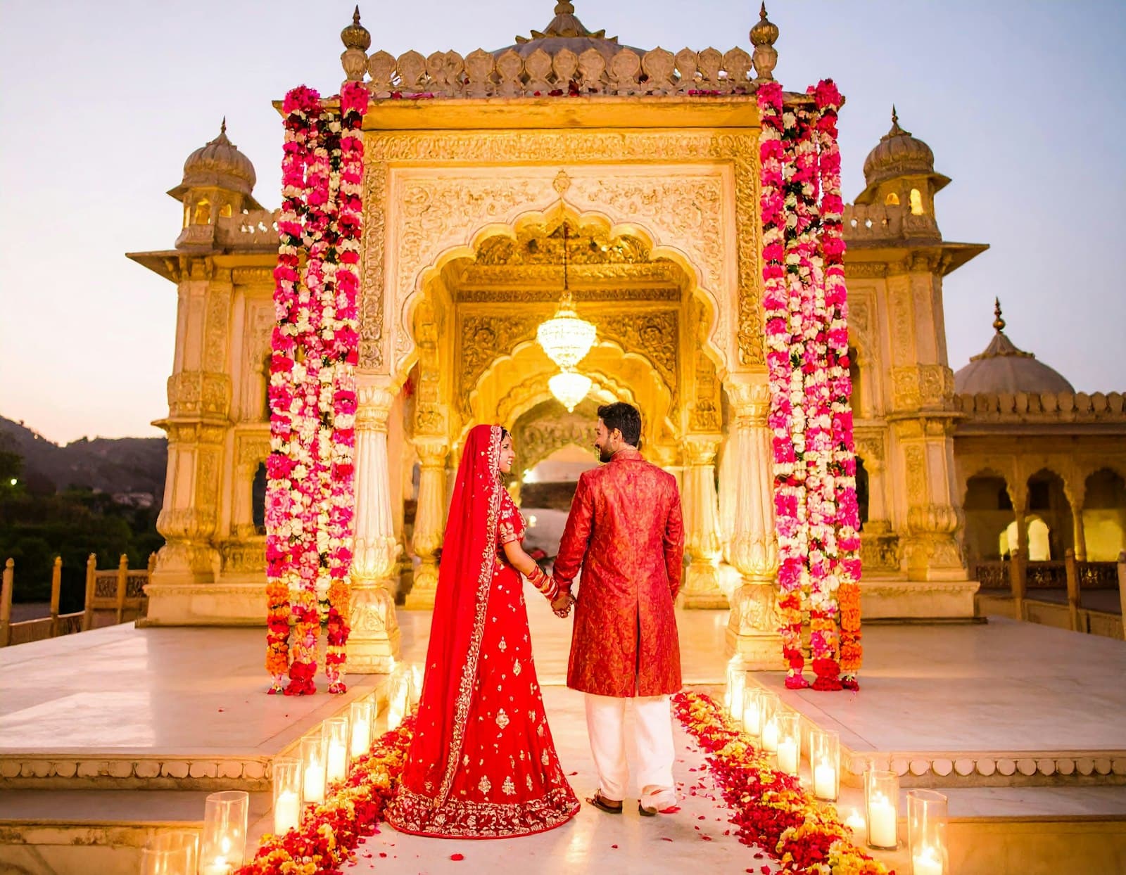 Couple in traditional red wedding attire standing before a carved archway framed with roses