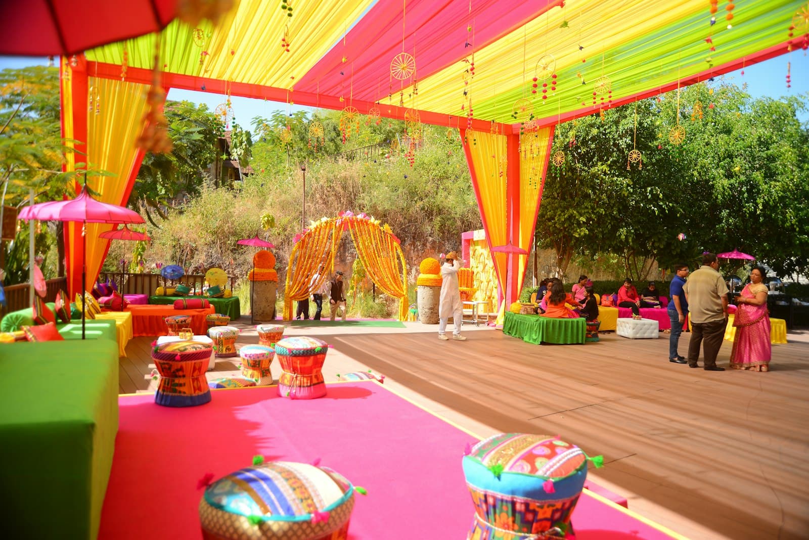 Mehendi setup with pink, yellow and green fabric canopies, floor cushions and umbrellas