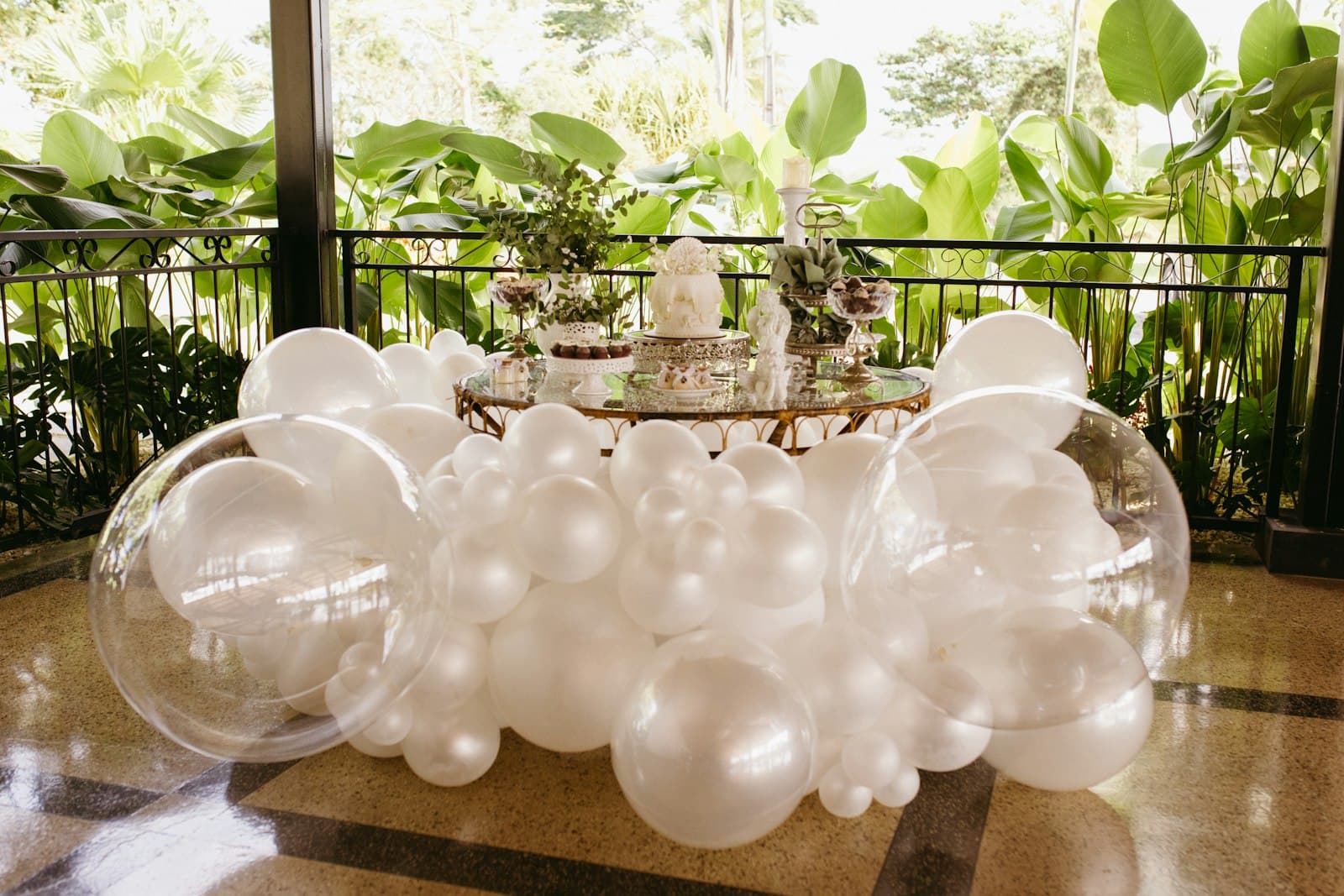 Dessert table surrounded by pearl-white and clear balloons on a garden terrace