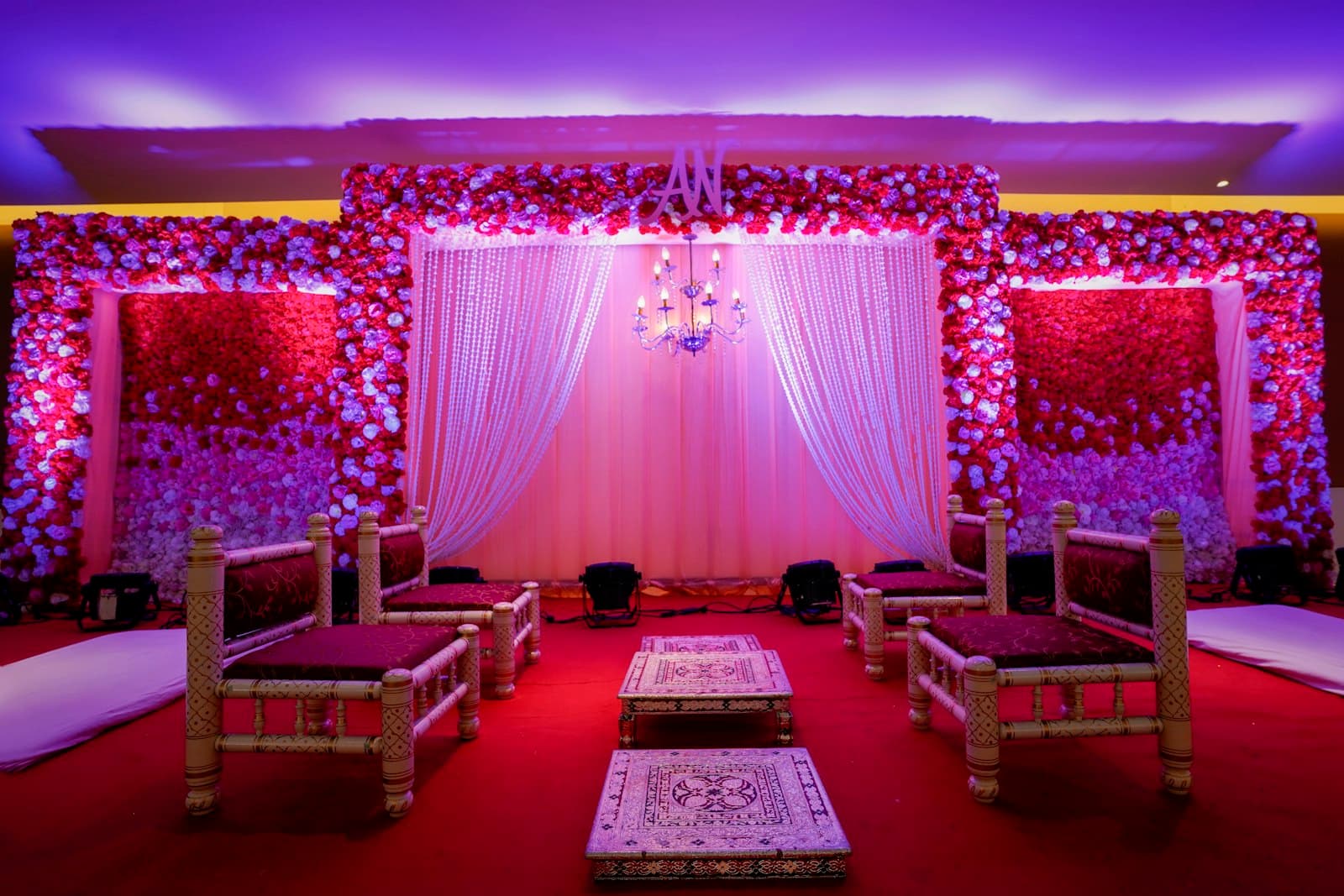 Reception stage with a wall of roses, sheer white drapes and carved seating